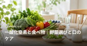 Plate of colorful fresh vegetables (broccoli, peppers, tomatoes, leafy greens) on a wooden table for a blog header about nutrition and oral care.